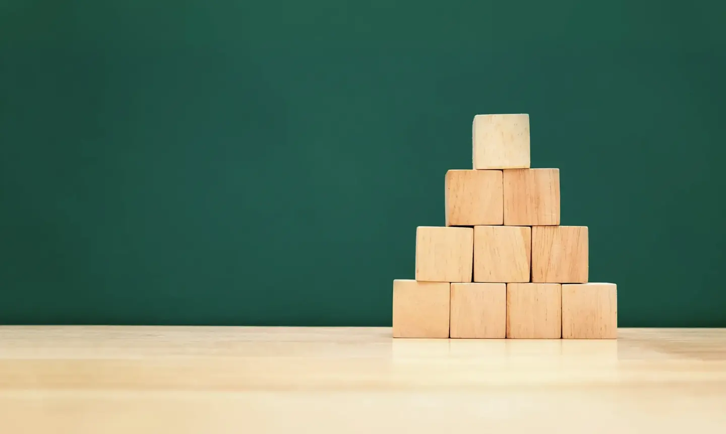 Houten bouwblokken gestapeld tot een piramide tegen een diepgroene achtergrond